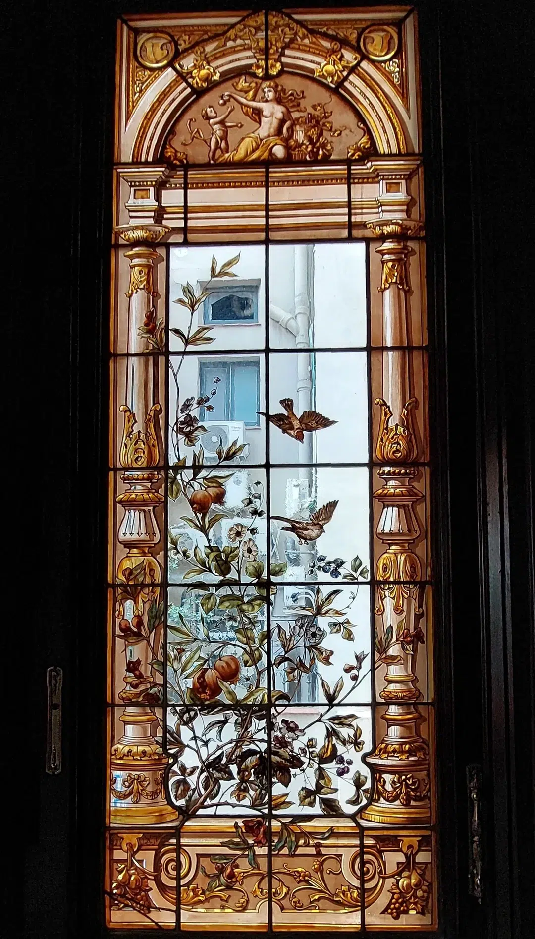 Detalle de pájaros y flores pintados en la vidriera modernista